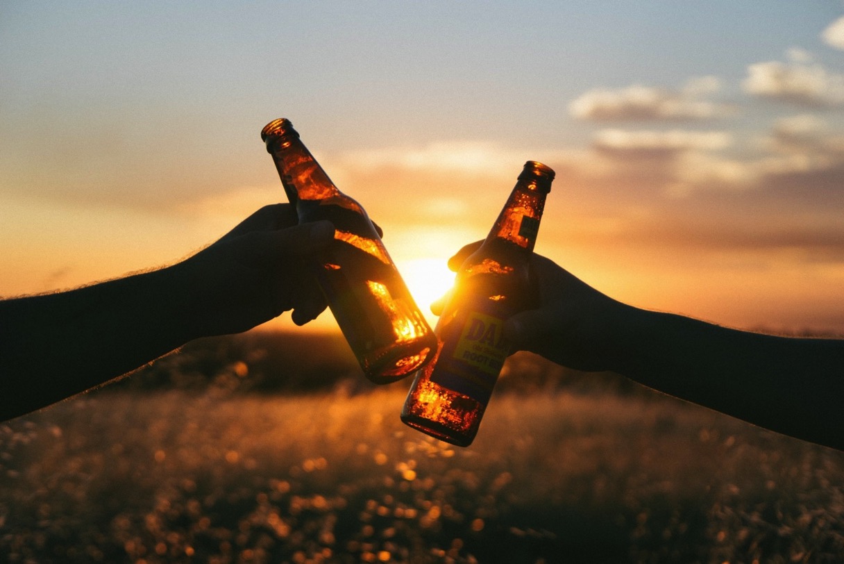 2 friends toasting with beer bottles in meadow at sunset