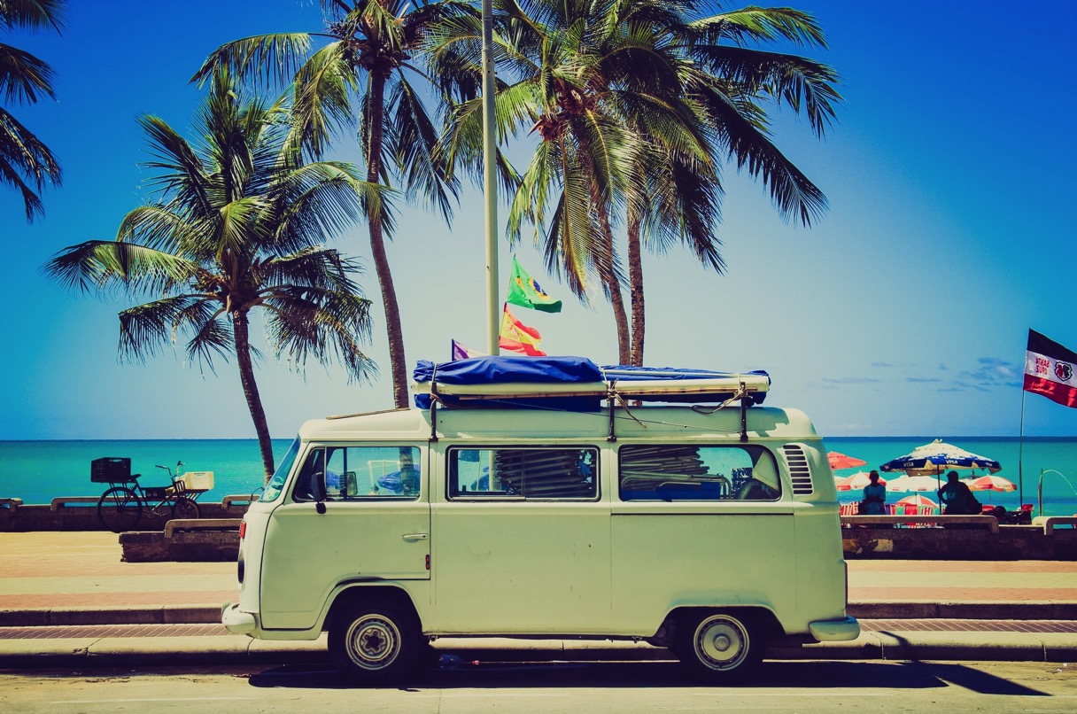 Green camper on promenade with palm tree and sea in background